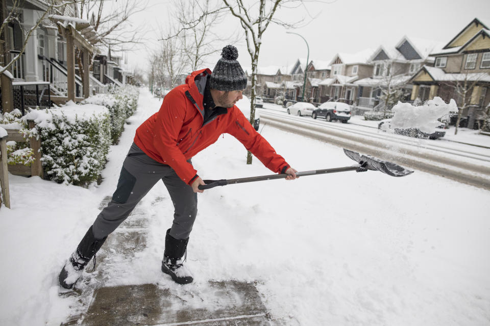 Side view shot of man shoveling snow off sidewalk in winter in suburb