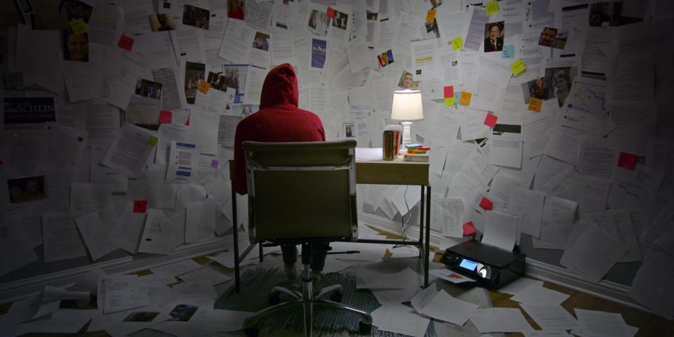 A woman sits at a desk decorated in newspaper clippings