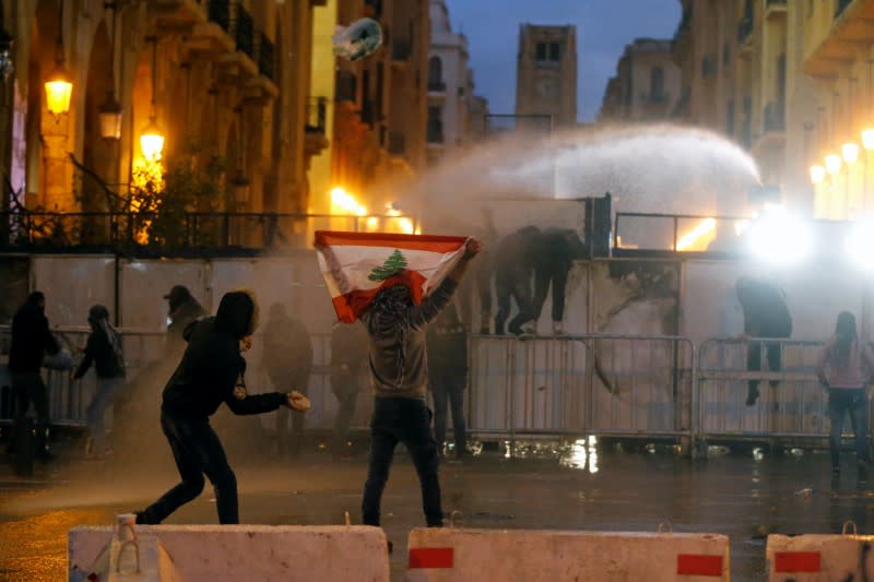 A demonstrator holds up a national flag as police use water cannon during a protest in Beirut