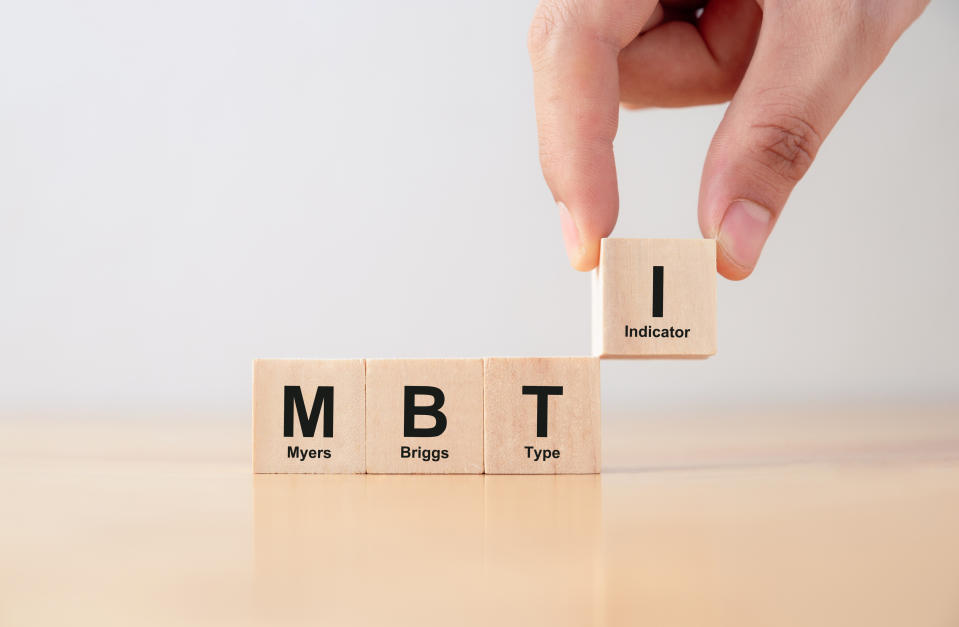 Wooden blocks on a table spell out "Myers-Briggs Type Indicator" as a hand places the final block labeled "I."