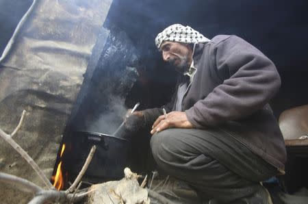 A Palestinian man prepares food over a cooking fire at his tent in the West Bank Beduin village of Almaleh, in the northern Jordan Valley January 6, 2015. REUTERS/Abed Omar Qusini