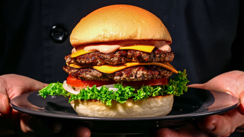 Hands holding plate with double cheeseburger