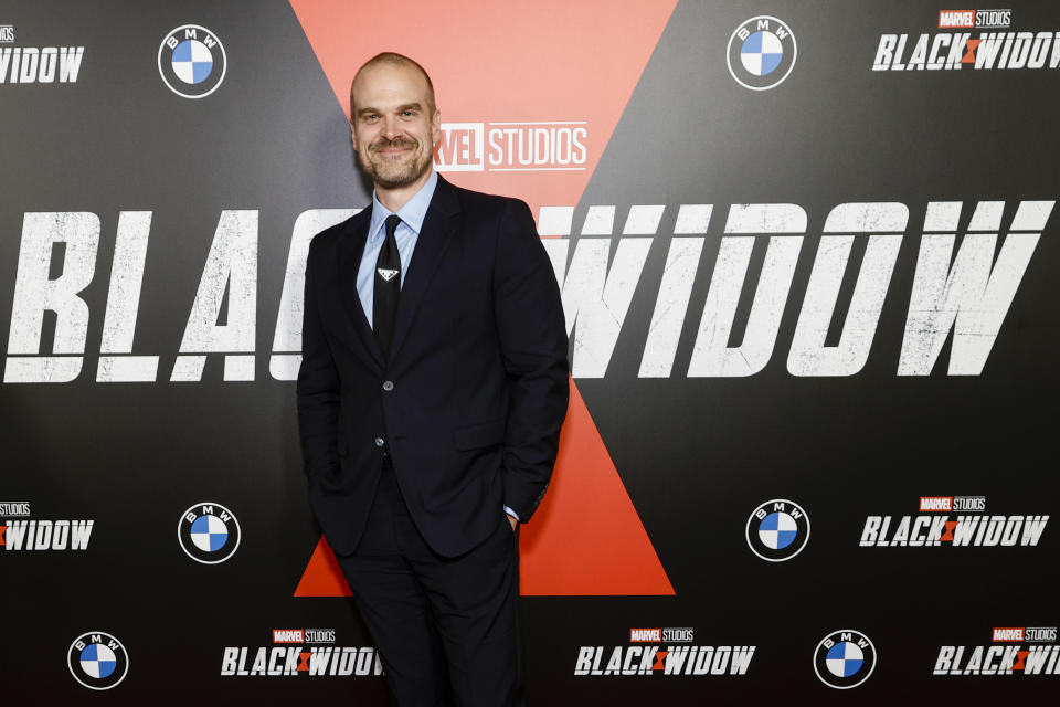 David smiling at the Black Widow premiere, wearing a black suit with a pale blue shirt and black tie