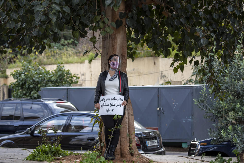 A protester holds a placard with Arabic that reads: "We raised them inch by inch and you killed their future, Leave," as she attends a march against the political leadership they blame for the economic, financial crisis and 4 Aug. Beirut blast, in Beirut, Lebanon, Saturday, March 20, 2021. (AP Photo/Hassan Ammar)