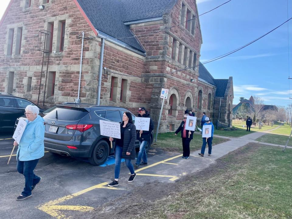 People carrying signs calling for justice for Tyson MacDonald walk outside the courthouse in Georgetown, P.E.I., on Friday morning.