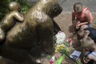 <p>Children pause at the feet of a gorilla statue where flowers and a sympathy card have been placed, outside the Gorilla World exhibit at the Cincinnati Zoo & Botanical Garden. <em>(AP Photo/John Minchillo)</em> </p>