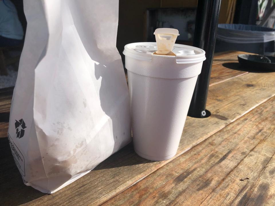 Greasy white paper bag next to a takeout styrofoam cup of coffee