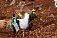 <p>A volunteer and soldiers carry a victim across the mud, days following the partial collapse of a hillside that swept away hundreds of homes in a neighborhood of the capital Freetown on Aug. 19, 2017.<br> (Photo: Seyllou/AFP/Getty Images) </p>