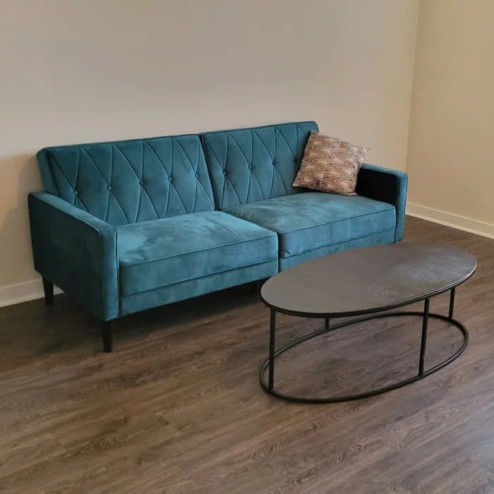 Reviewer's photo of the velvet tufted sofa in the color turquoise with cushions and a round metal coffee table in a living room setting