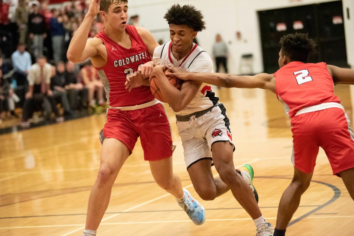 Marshall senior Nauvion Burnett (4) goes in for a layup as Coldwater junior Donte Work (24) and senior Lu Lebron (2) guard him at Marshall High School on Friday, Jan. 7, 2022. Marshall defeated Coldwater 64-55.