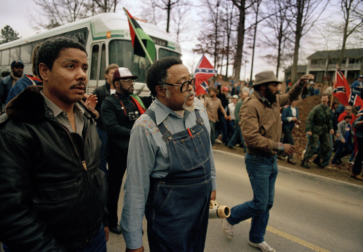 Atlanta City Councilman Hosea Williams, wearing overalls, leads a 1987 march in Cumming against efforts to keep Forsyth County all white, as a crowd waves Confederate flags and jeers. 