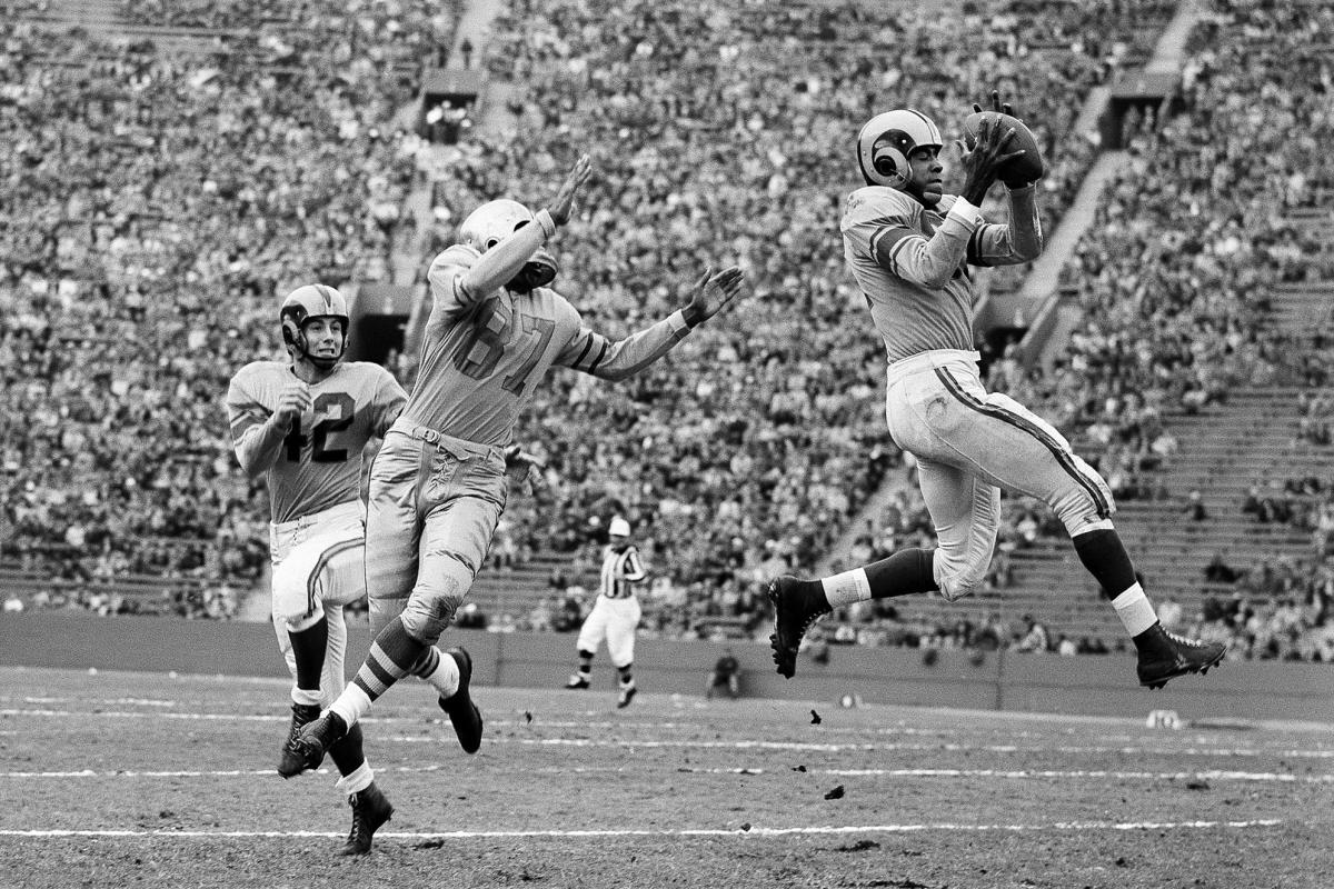 FILE - In this Dec. 8, 1953, file photo, Cleveland Browns coach Paul Brown  checks the protective mask of his quarterback Otto Graham. In 1950, the NFL  merged with the All-America Football