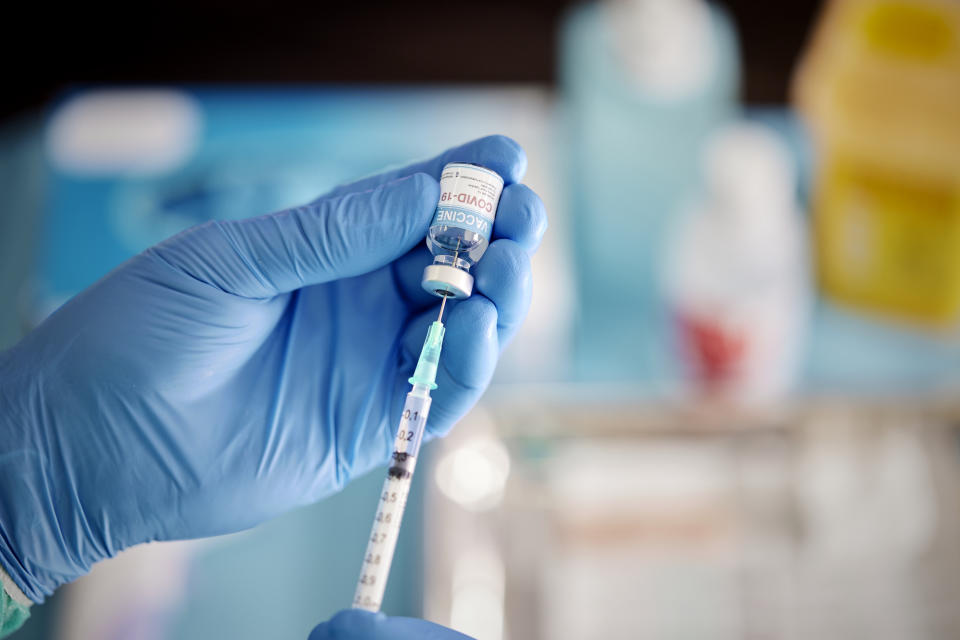 A health-care worker wearing blue surgical gloves pulls a COVID-19 vaccine liquid from a vial to vaccinate a patient