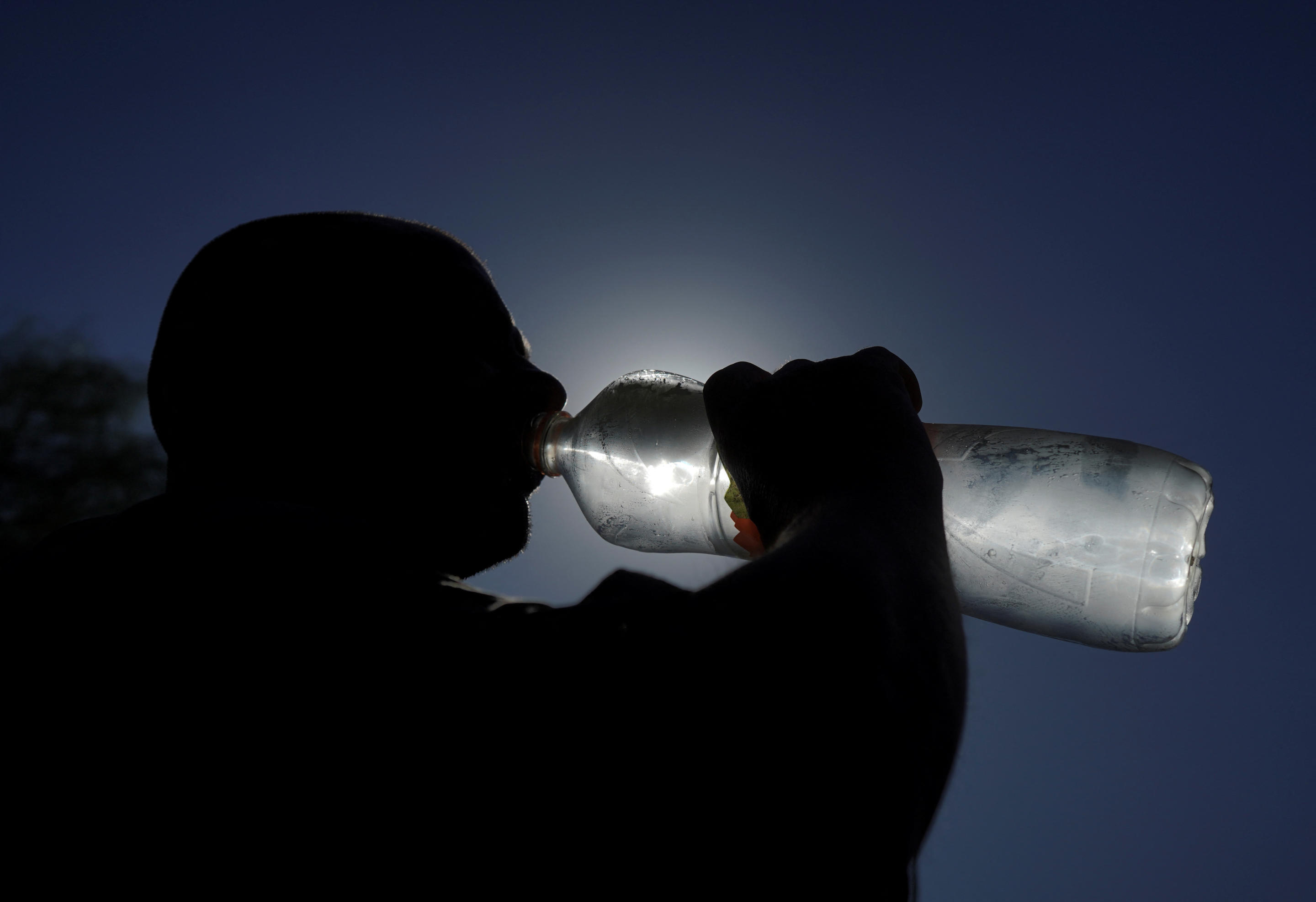 A silhouette of a man drinking from a large water bottle. 