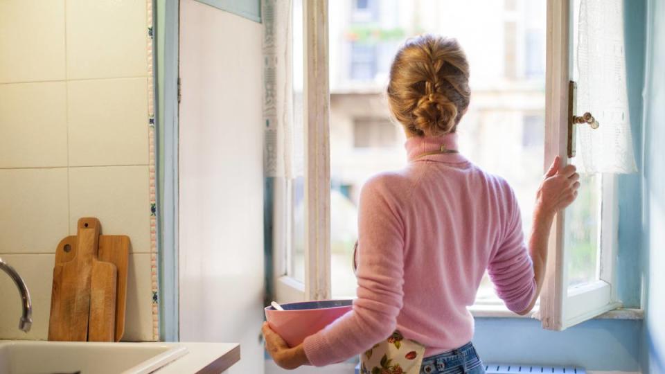 how to get burnt smell out of house: Woman opening kitchen window, holding a bowl