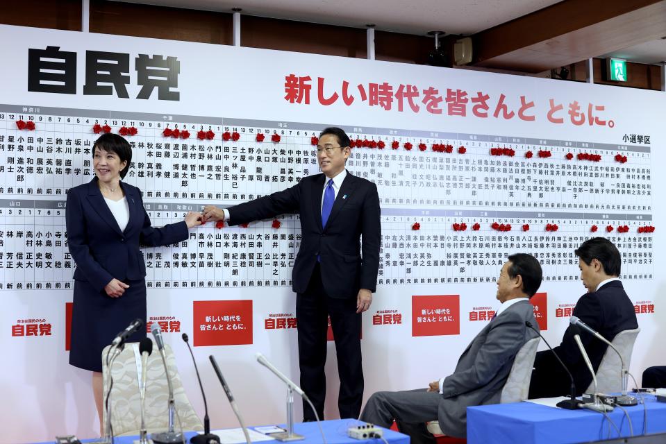 Japan's Prime Minister and ruling Liberal Democratic Party leader Fumio Kishida, 2nd left, and former Minister of the Internal Affairs and a senior member of the party, Sanae Takaichi, left, put a rosette on her name after winning a seat at the lower house parliament, at the party headquarters in Tokyo, Sunday, Oct. 31, 2021. Japanese Prime Minister Fumio Kishida’s governing coalition is expected to keep a majority in a parliamentary election Sunday but will lose some seats in a setback for his weeks-old government grappling with a coronavirus-battered economy and regional security challenges, according to exit polls. (Behrouz Mehri, Pool via AP)