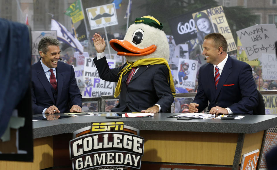 FILE - In this Oct. 12, 2013, file photo, ESPN College GameDay host Lee Corso, center, wears an Oregon Duck mascot head as he makes his prediction of an Oregon win over Washington in an NCAA college football game, during College GameDay's broadcast from Red Square on the University of Washington campus in Seattle. At left is co-host Chris Fowler, and at right is co-host Kirk Herbstreit. ESPN has agreed to a multiyear contract extension with Lee Corso, the 81-year-old star of "College GameDay." Corso joined ESPN in 1987 and has been part of the popular college football Saturday pregame show ever since.  (AP Photo/Ted S. Warren, File)