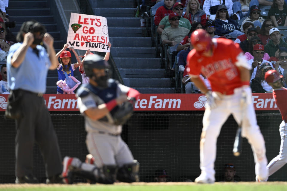 Two young fans hold a sign as Los Angeles Angels' Mike Trout, right, bats next to Boston Red Sox catcher Reese McGuire during the eighth inning of a baseball game in Anaheim, Calif., Sunday, April 7, 2024. (AP Photo/Alex Gallardo)