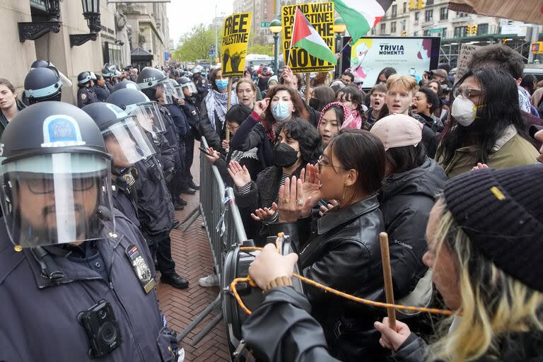 Agentes de policía de la ciudad de Nueva York con equipo antidisturbios hacen guardia mientras los manifestantes cantan consignas frente al campus de la Universidad de Columbia, el jueves 18 de abril de 2024