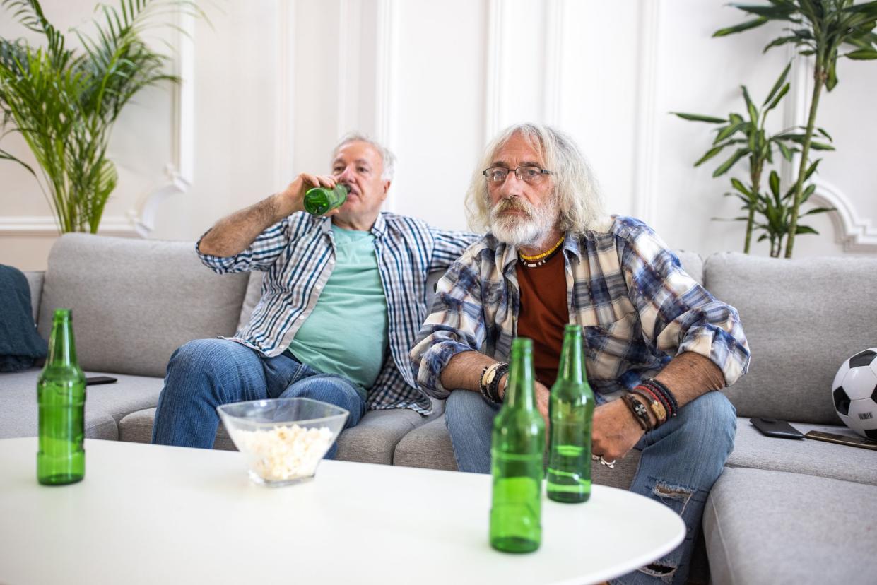 Senior friends watching tv and drinking beer in living room