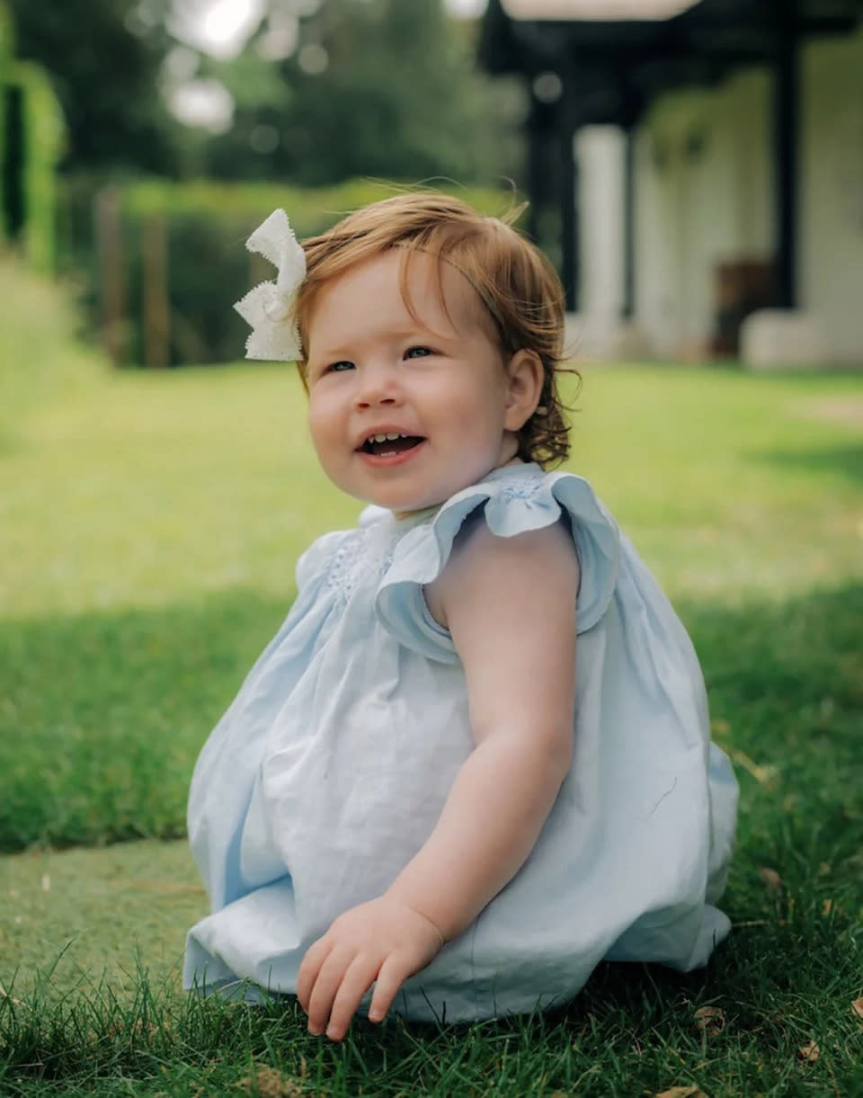 Lilibet sits on the grass in a blue dress. 