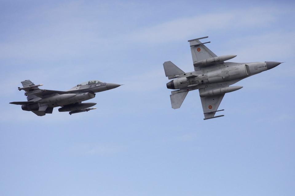 Two F-16 perform fly-bys against a blue sky