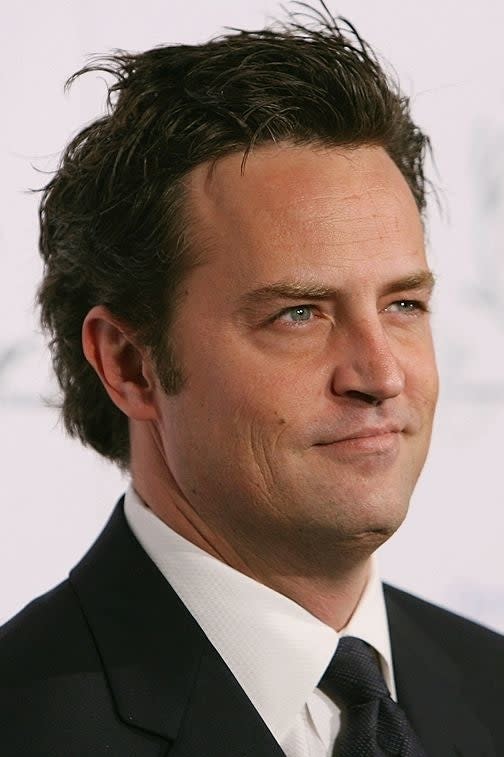 Matthew Perry in a dark suit and tie at an event, looking to the side