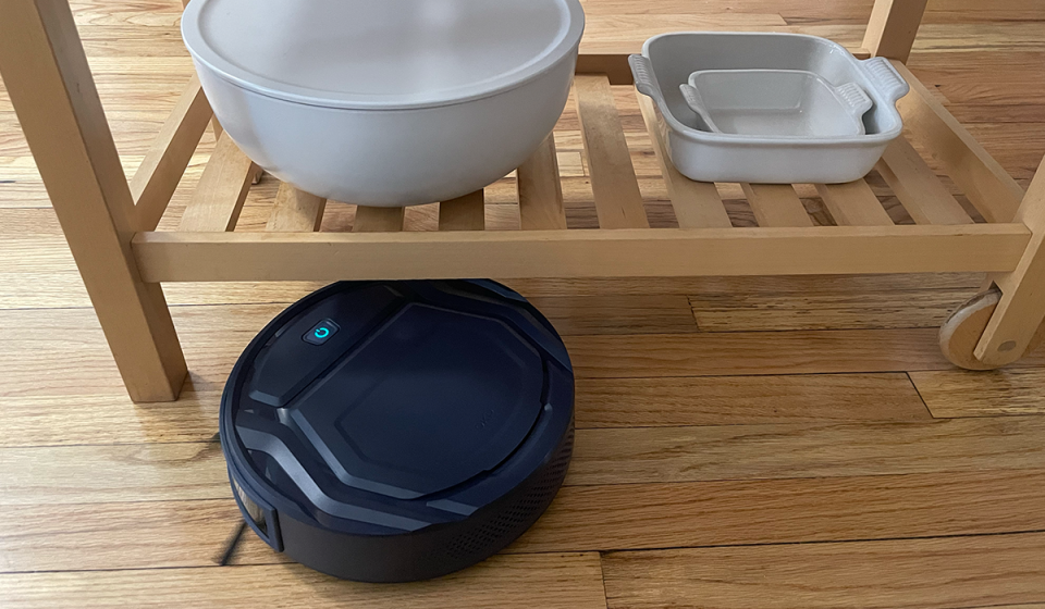 The OKP K2 Robot Vacuum Cleaner is shown vacuuming a narrow furniture space.