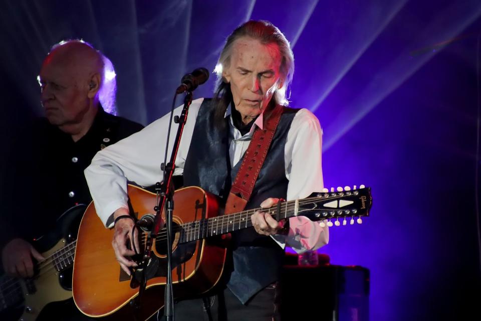 gordon lightfoot sitting down and playing guitar behind a microphone