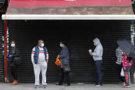 Customers queue outside a retail shop in front of a closed shop as coronavirus restrictions on non-essential retailers were lifted in London, Friday, June 19, 2020. Retailers see a much-needed boost in sales this month compared with the record lows in April as lockdown turned thriving high streets into ghost towns. (AP Photo/Frank Augstein)