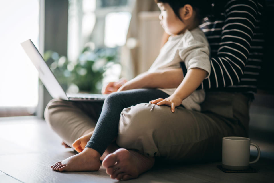 Cropped shot of a young Asian mother using laptop and working from home while taking care of little daughter in self isolation during the Covid-19 health crisis