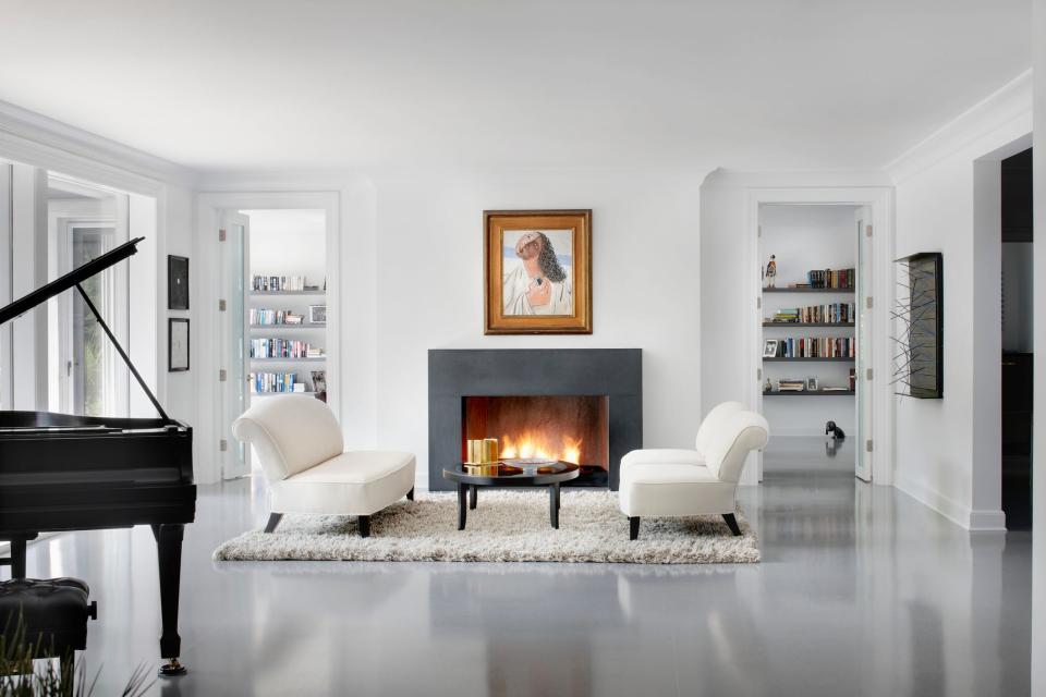 Two white chairs on white rug in front of a black fireplace with white walls