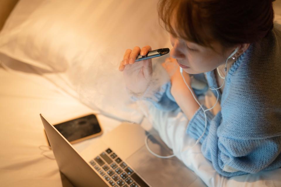 Young woman vaping an electronic cigarette for relax while working at night