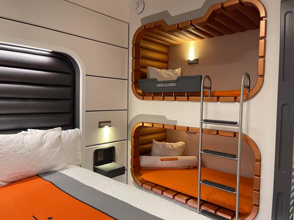 the in-wall bunk beds in a starcruiser room with orange bedding and a ladder