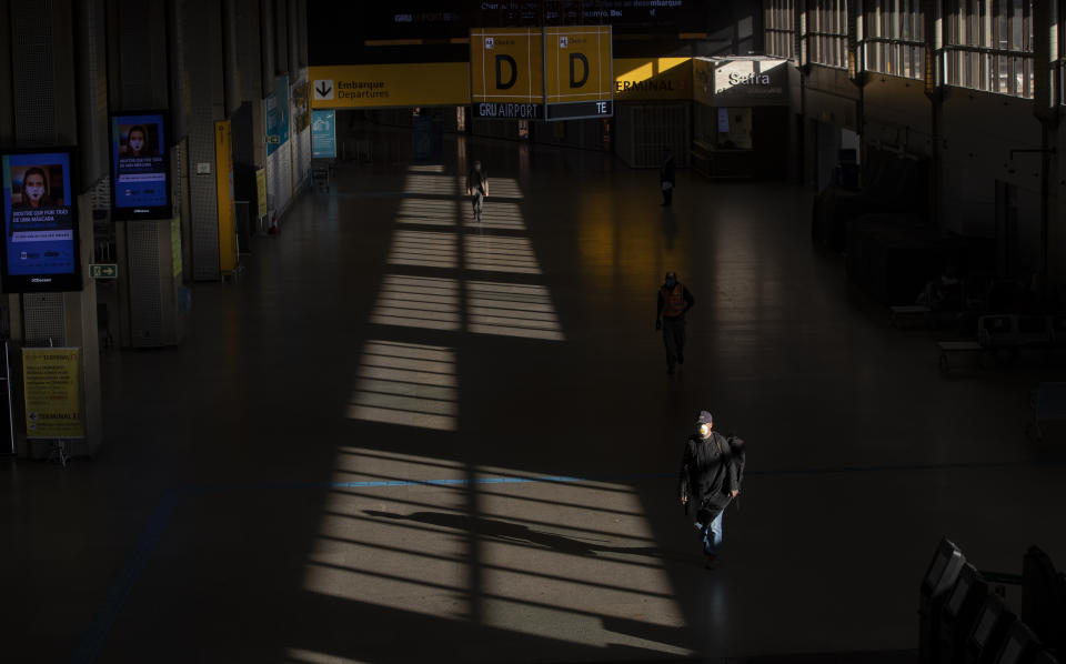 A few people walk through an empty corridor inside the Sao Paulo International Airport in Guarulhos, Brazil, Wednesday, May 27, 2020. According to the airport administration, Brazil's busiest airport has had an average reduction of 85% in flights, due to the COVID-19 pandemic. (AP Photo/Andre Penner)