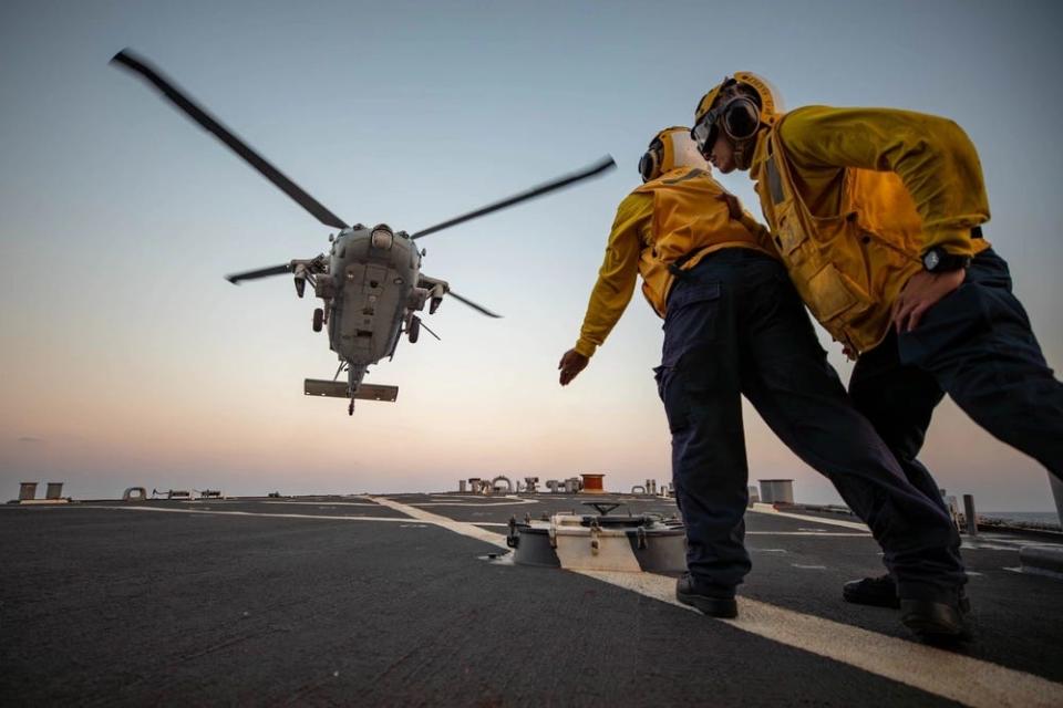 A photo of two people in yellow long sleeves and yellow vests looking at a helicopter.