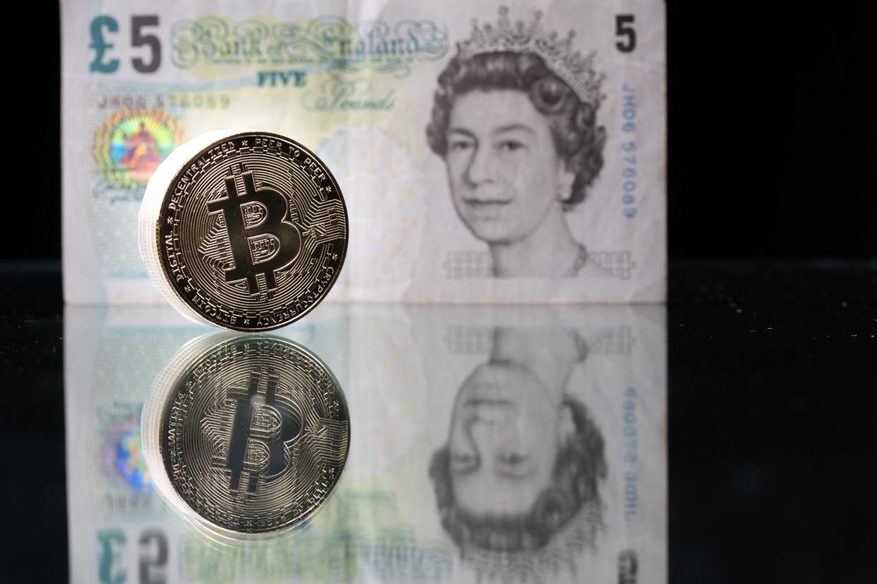 Photo taken in Paris shows a physical imitation of the Bitcoin pictured with a British five pound bank note (AFP via Getty Images)