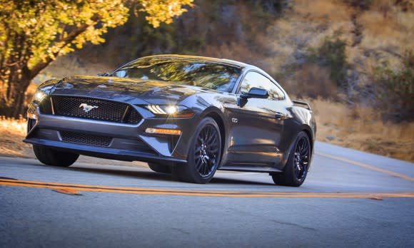 A 2018 Ford Mustang fastback in a dark metallic gray, on a country road.