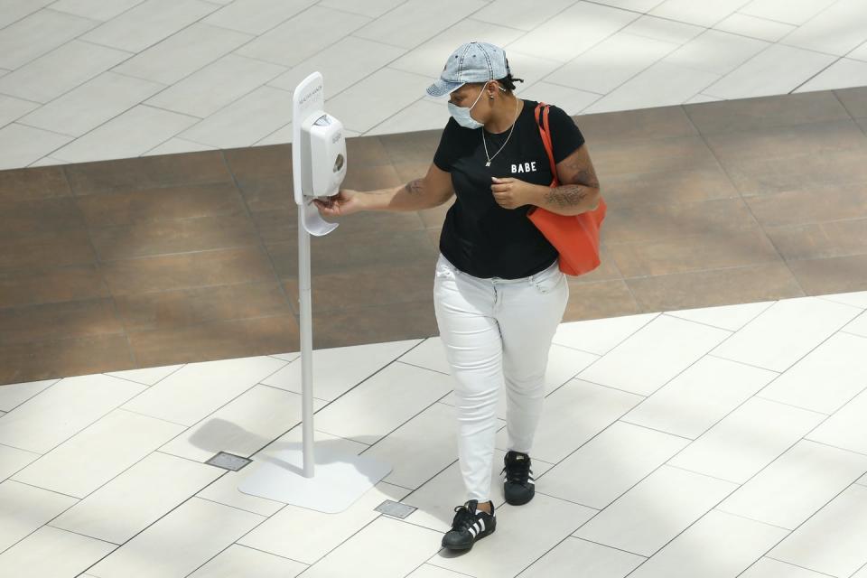 A woman wearing a mask using a hand sanitizer dispenser.