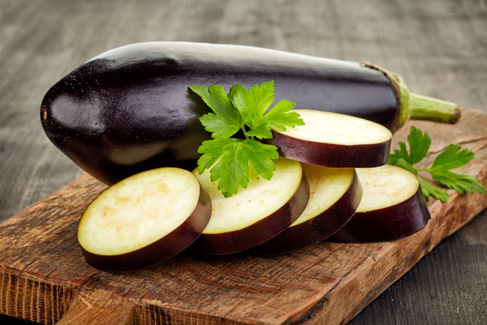 A whole eggplant and half sliced eggplant on a cutting board 