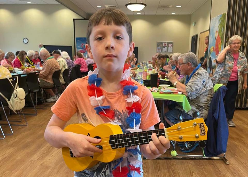 Special guest Miles Robb, 8, takes his ukulele playing seriously at the luau at Karns Senior Center Tuesday, June 7, 2022.