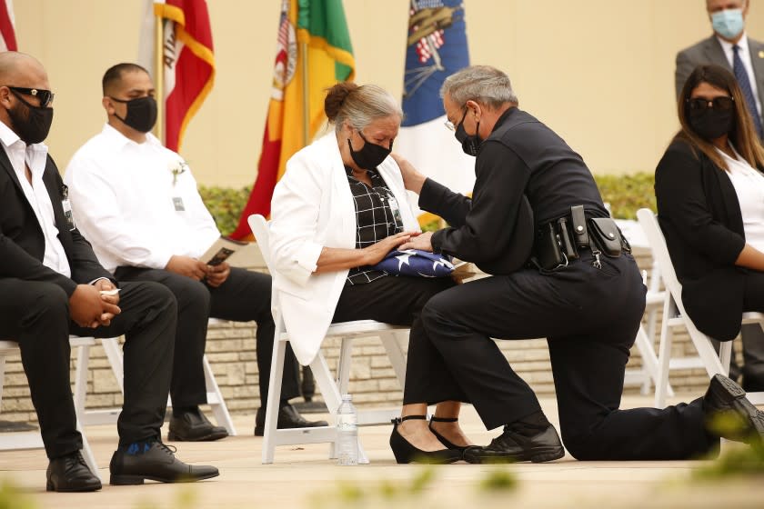 LOS ANGELES, CA - AUGUST 06: Chief of the Los Angeles Police Department Michel R Moore presents the United States flag to Maria Martinez, mother of LAPD Officer Valentin Martinez, the agency's first sworn employee to die of complications from the COVID-19. The social distance memory service was held at Forest Lawn Hollywood Hills' Hall of Liberty this morning. Martinez was a 13-year veteran of the department and is presumed to have contacted the virus on duty. He was 45 when he died on July 24, 2020, leaving behind his mother, Maria Martinez, his siblings and his domestic partner, Megan Flynn, who is pregnant with their twins. Los Angeles on Thursday, Aug. 6, 2020 in Los Angeles, CA. (Al Seib / Los Angeles Times)