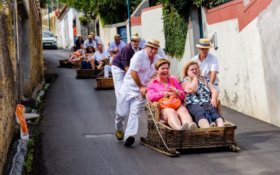 Tourists being pushed downhill in a wicker toboggan