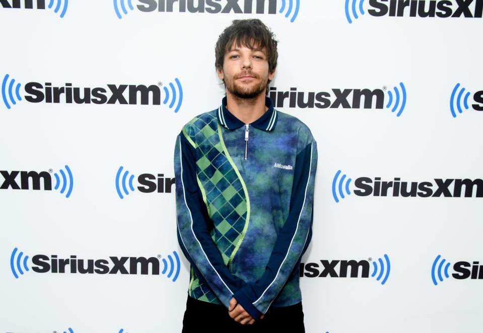 Louis Tomlinson in a blue pattern jacket in front of a "SiriusXM" backdrop