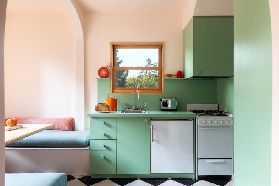 This renovated space was designed to honor the building’s past, with a contemporary twist. In the mini kitchen, custom mint-green cabinetry and classic black-and-white linoleum floors live alongside an airy, peach-hued dining area with built-in banquette seating, arched detailing, and modern lighting.