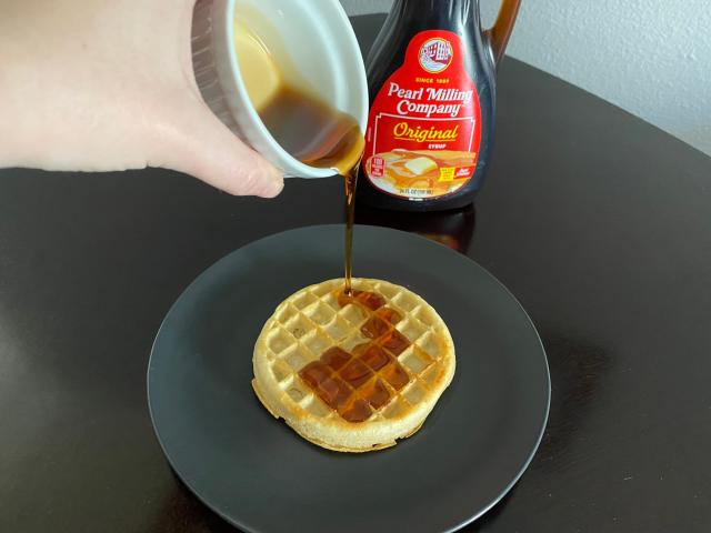 hand pouring white ramekin of pearl milling company syrup onto a frozen waffle