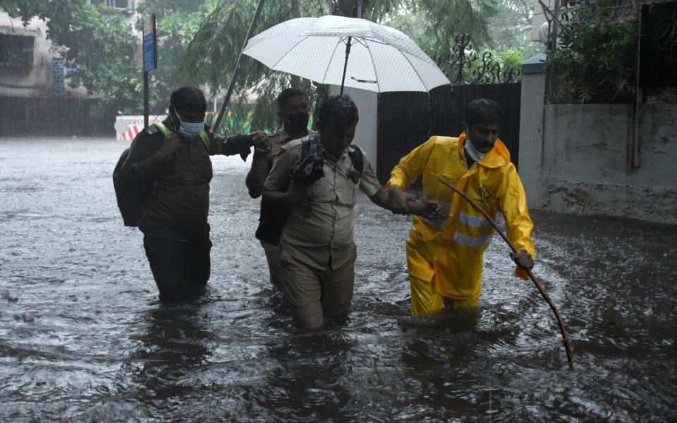 A policeman helps a driver cross a flooded street after his public transport bus became stuck due to heavy rain hit Mumbai - STR/EPA-EFE/Shutterstock