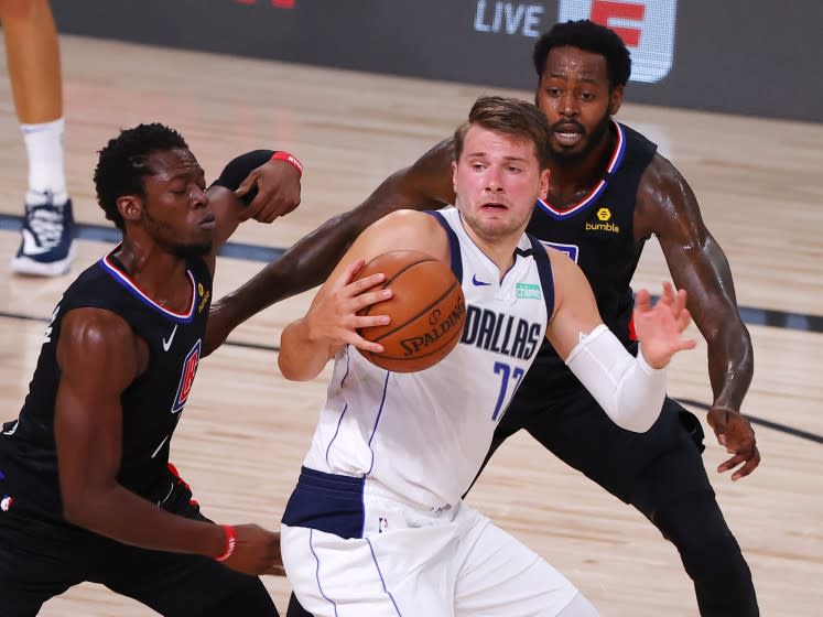 Dallas Mavericks' Luka Doncic (77) is pressured by Los Angeles Clippers' Reggie Jackson (1) and JaMychal Green, right, during the third quarter of Game 1 of an NBA basketball first-round playoff series, Monday, Aug. 17, 2020, in Lake Buena Vista, Fla. (Kevin C. Cox/Pool Photo via AP)