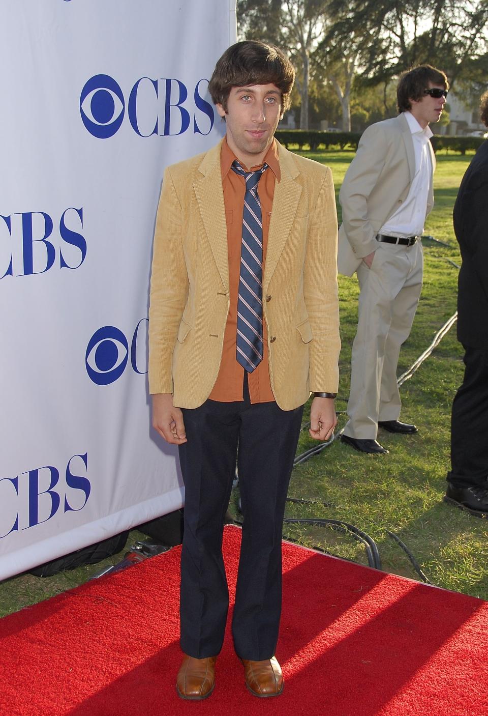 wearing a blazer and bright button-down with a tie and his hair cut into a bowl cut