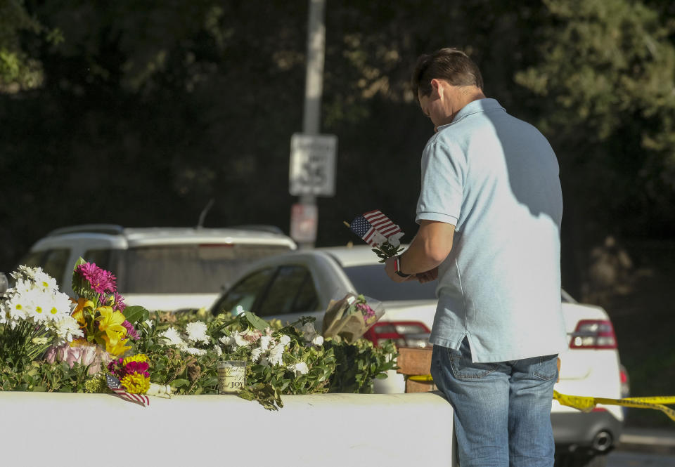 Brian White places a U.S. flag with a flower near the scene of a mass shooting Thursday, Nov. 8, 2018, in Thousand Oaks, Calif., after a gunman opened fire Wednesday evening inside a country music bar, killing multiple people including a responding sheriff's sergeant. (AP Photo/Ringo H.W. Chiu)